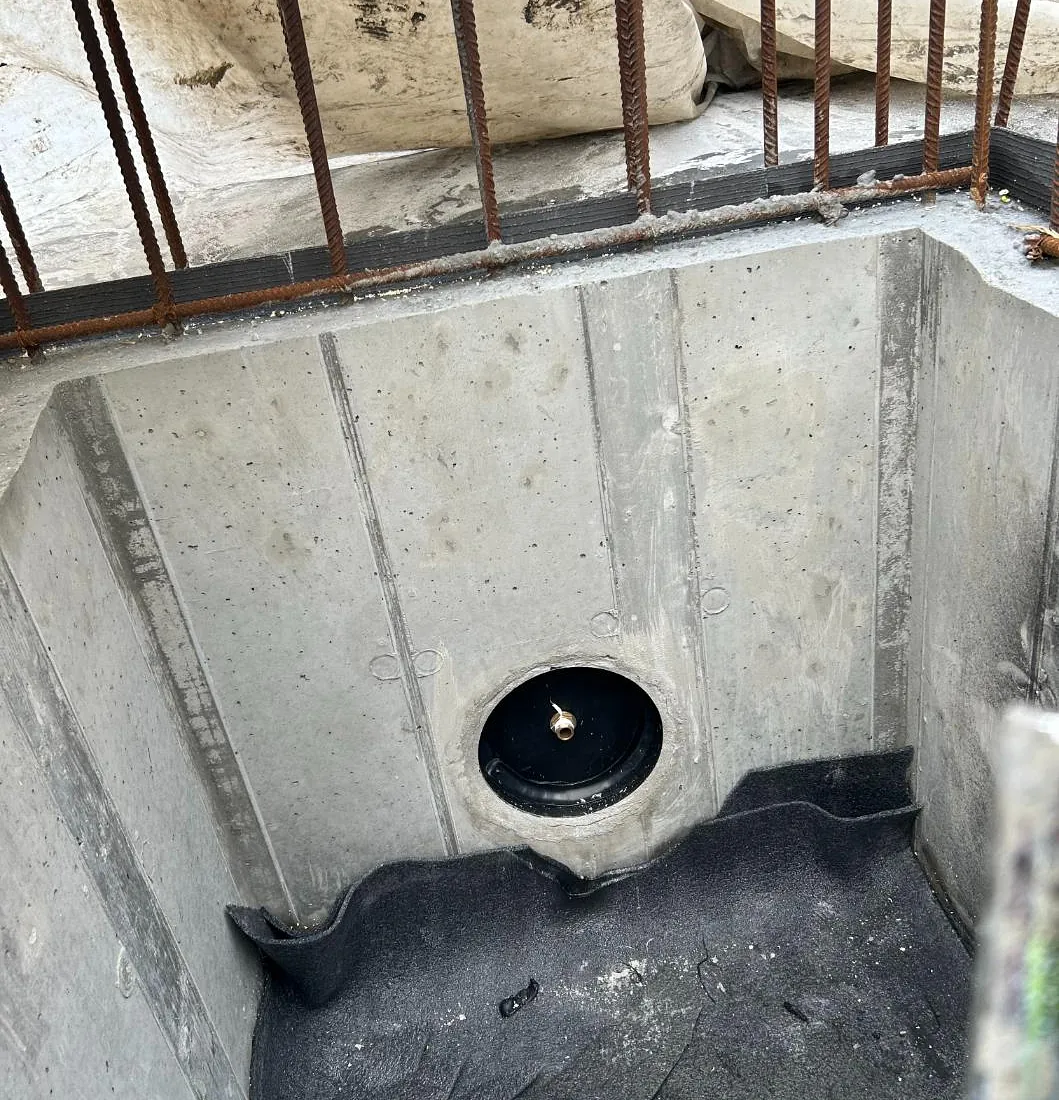 Betongkum med montert gjennomføring og svart membran nederst, armeringsjern synlig.
