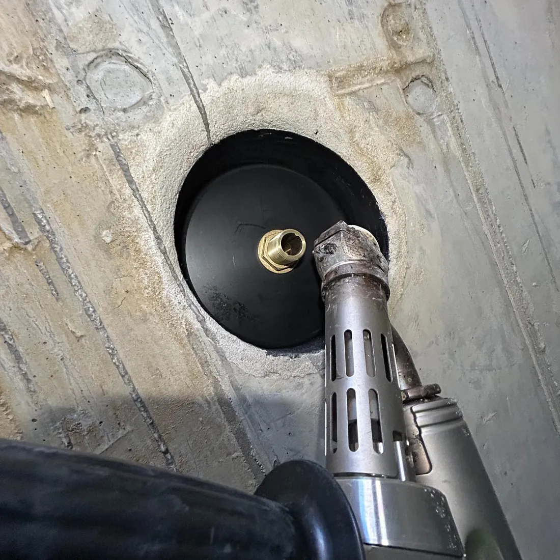 Nærbilde av dyse og messingkobling montert i et hull i betongvegg.